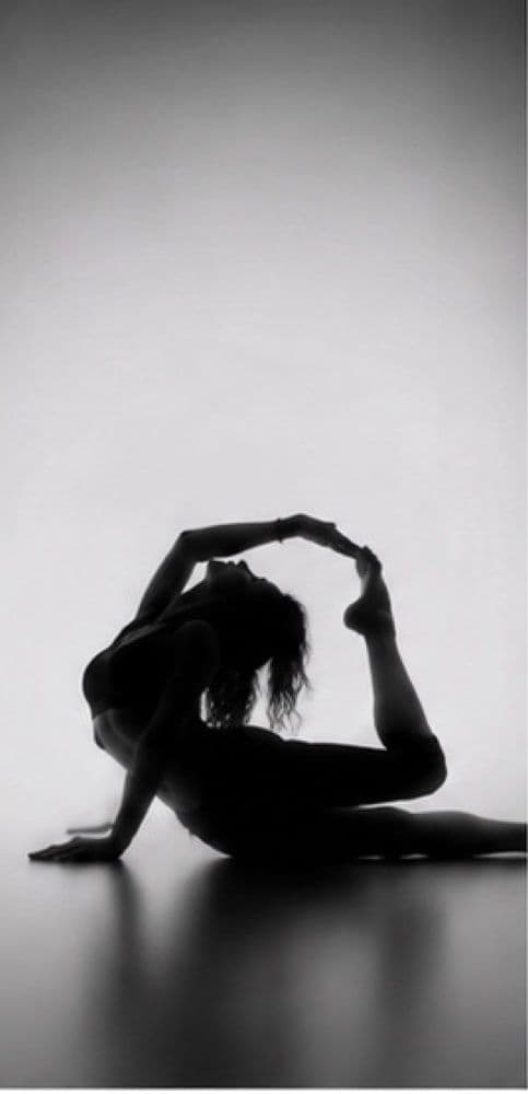 Silhouette d’une danseuse au sol, les mains rejoignant son pied levé